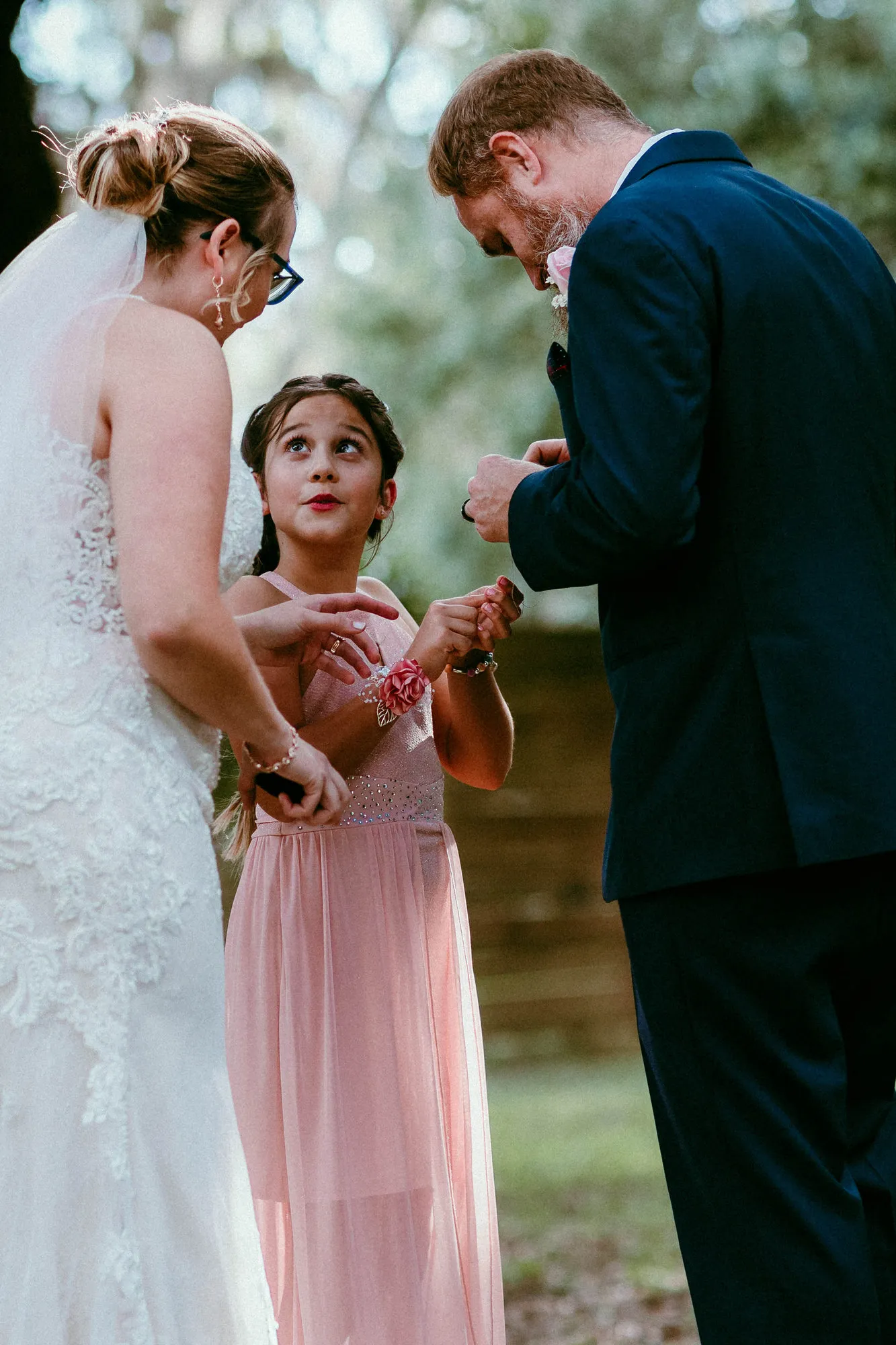 Girl in a pink dress looking up between the bride and groom during the ceremony