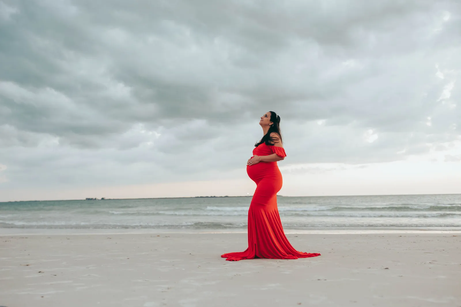 Expectant mother in red looking up at the clouds, in profile