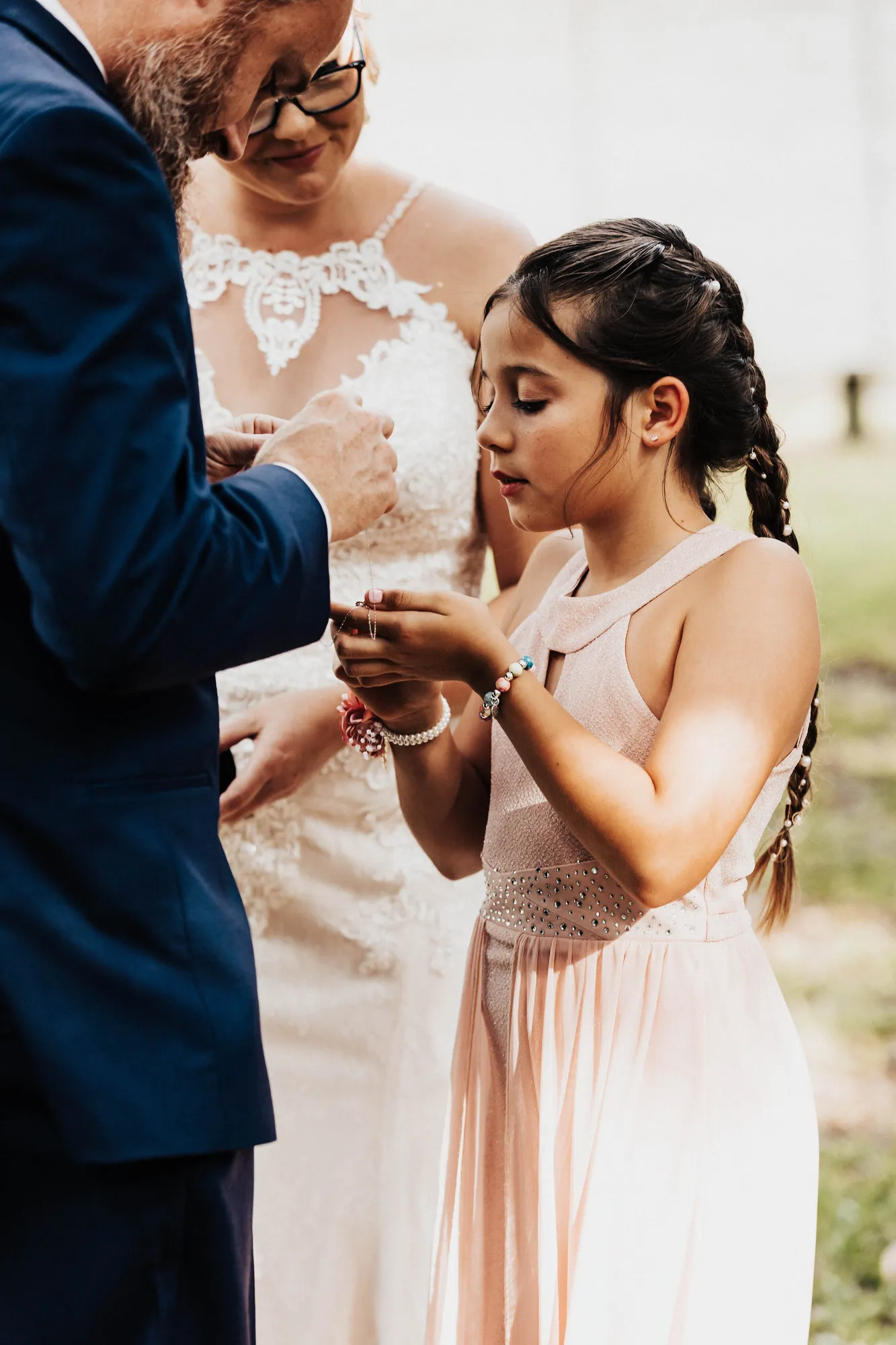 Groom placing a bracelet on the girl's wrist as the bride looks on