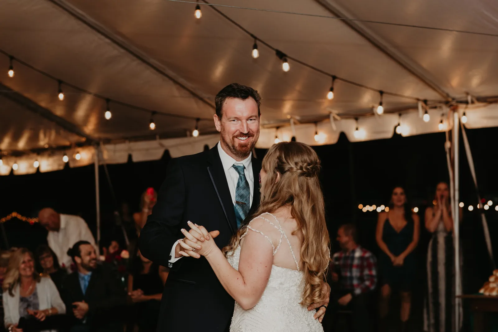 Groom smiling as he dances with his bride under the tent lights