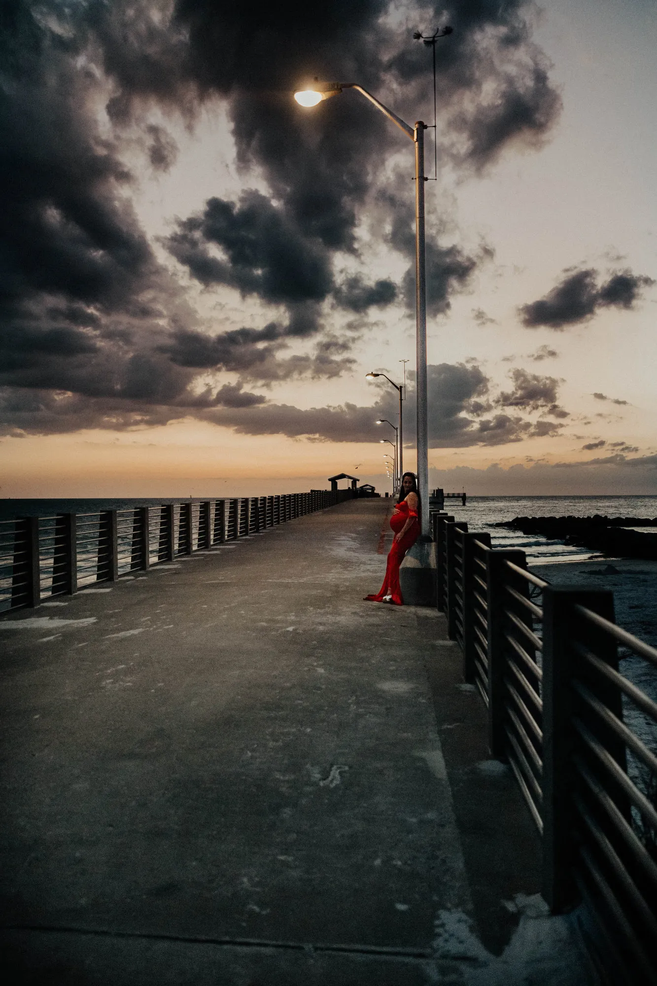 Expectant mother leaning on the pier railing under a streetlight and dark clouds