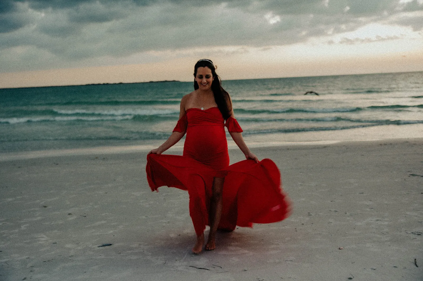 Expectant mother laughing as she swishes the skirt of her red gown