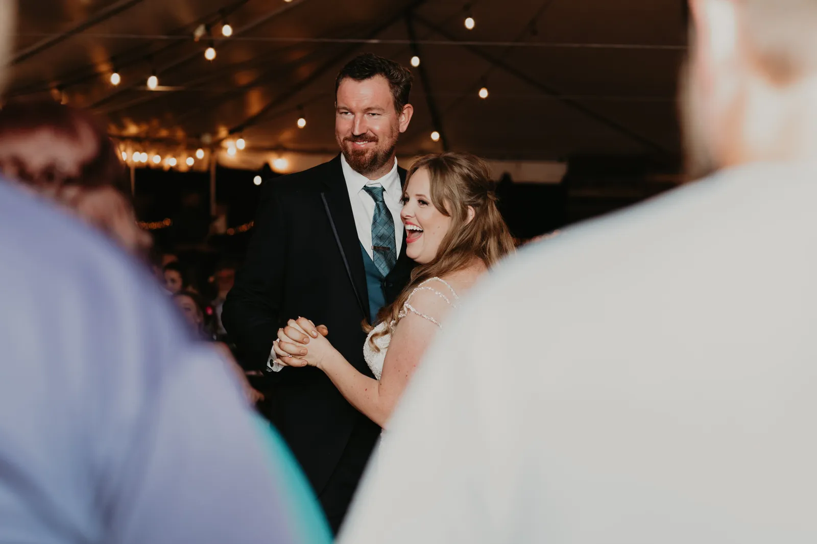 Bride laughing during the first dance, framed by guests' shoulders