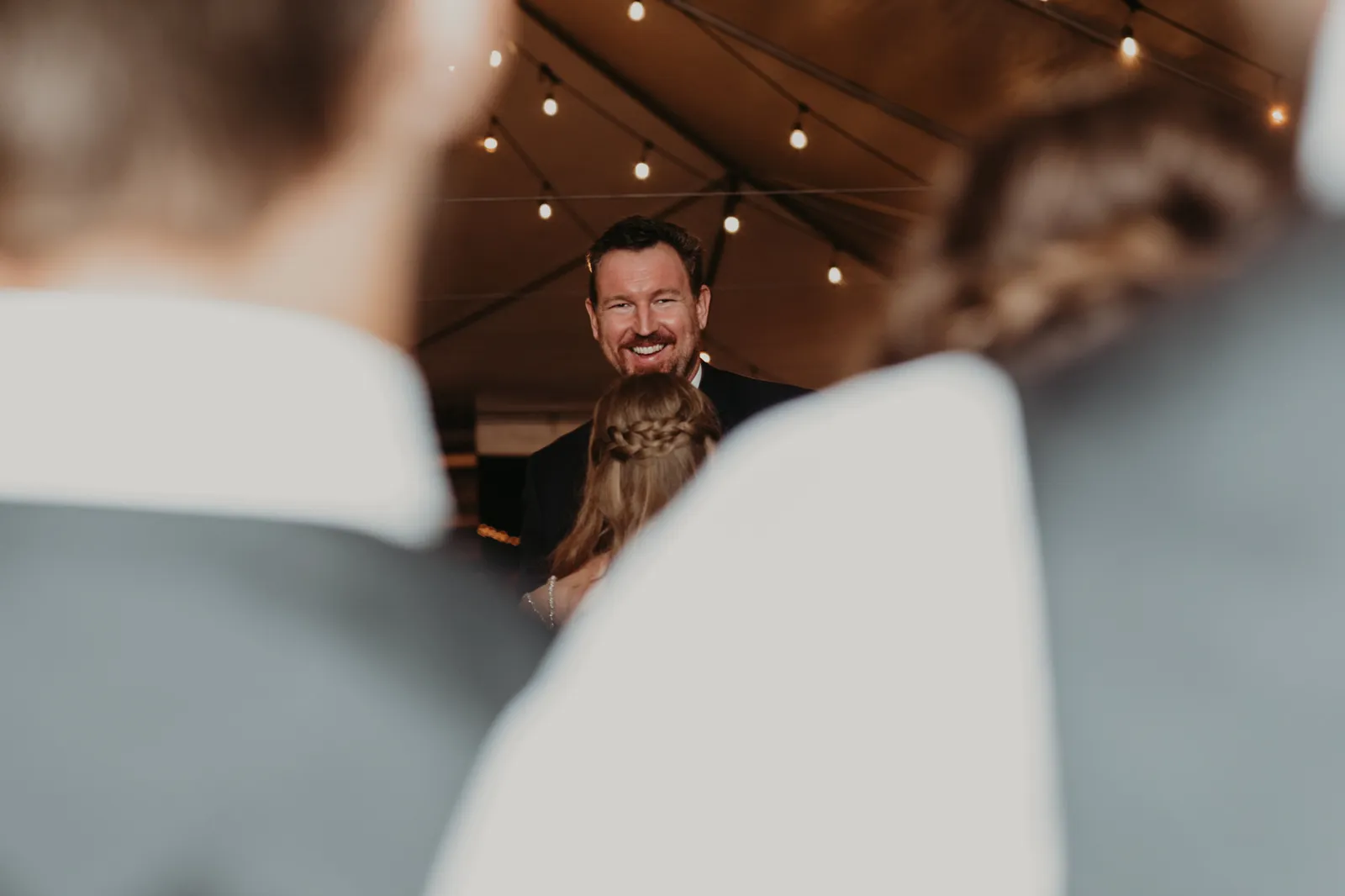 Groom smiling over the bride's shoulder, seen between two guests
