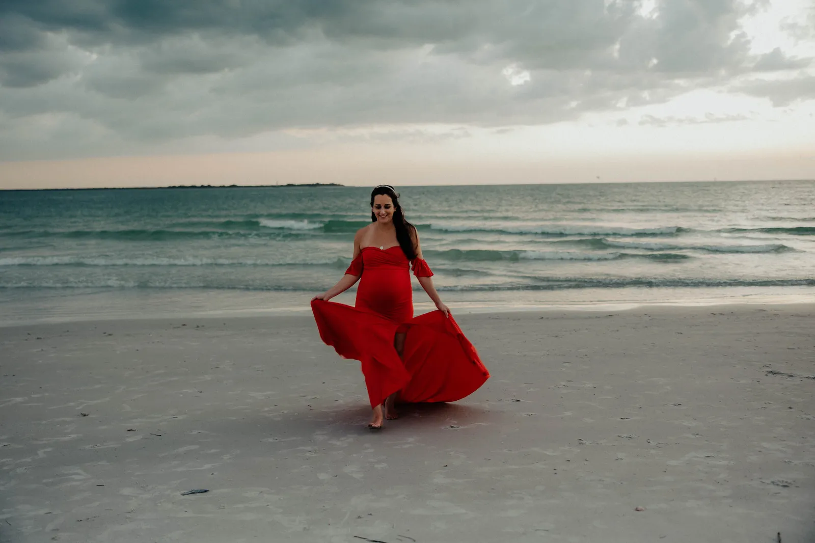 Expectant mother twirling her red gown on the sand