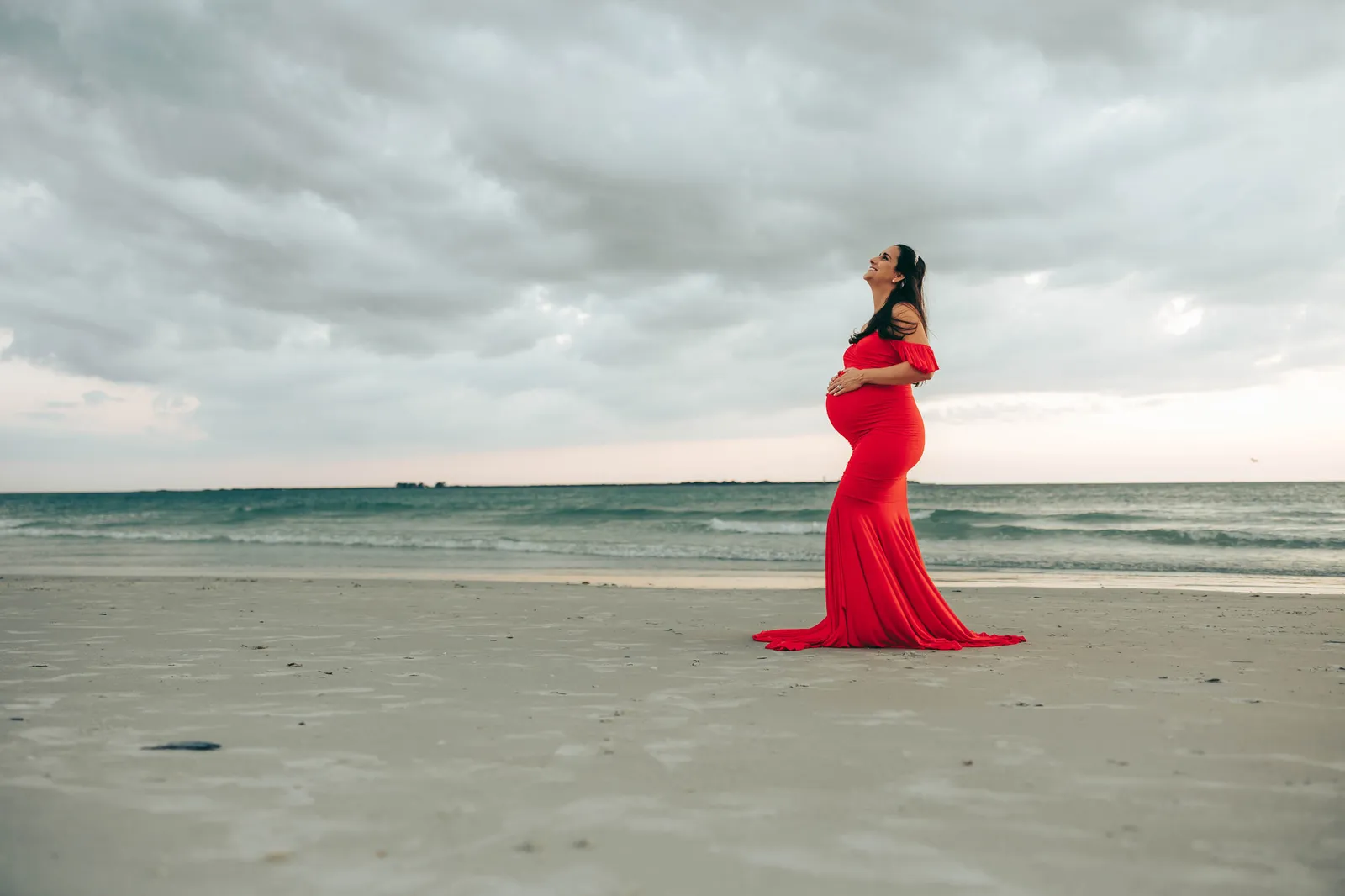 Expectant mother in red tilting her head back, storm clouds overhead