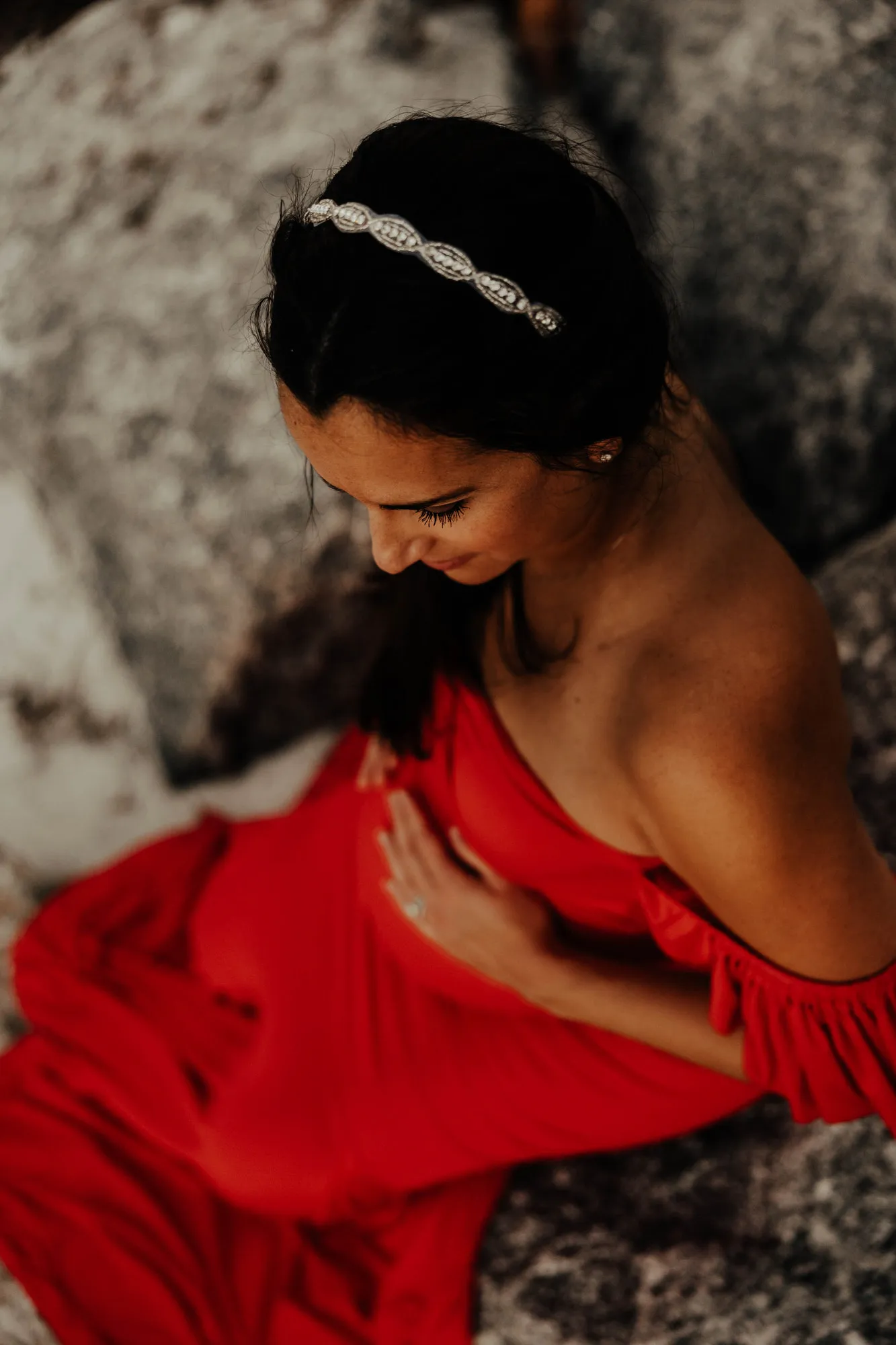 Expectant mother seen from above, her hand on her bump, sitting on the rocks