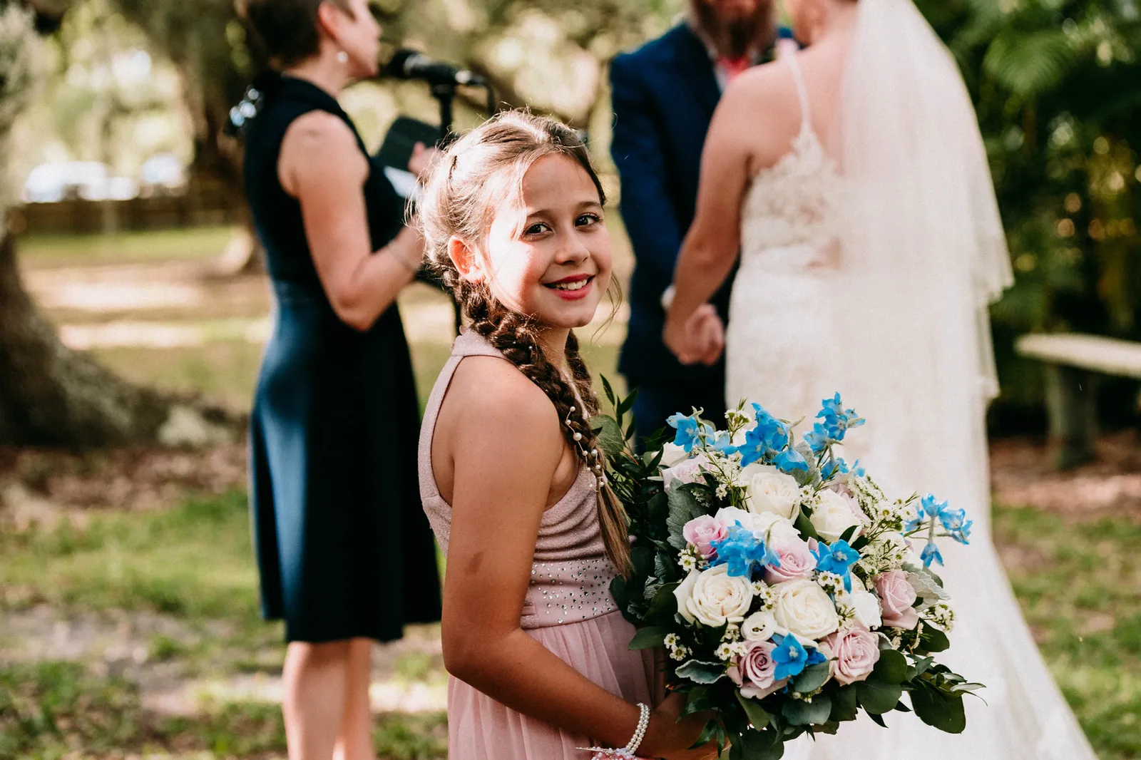 Girl with braids smiling back at the camera, holding the bride's blue and white bouquet