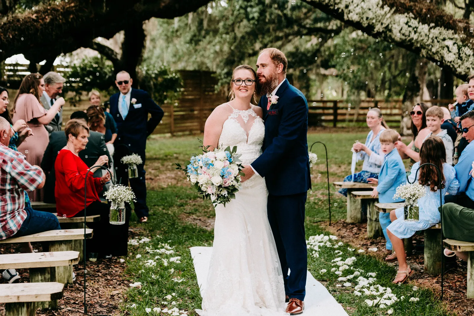 Bride and groom standing arm in arm in the aisle as guests look on