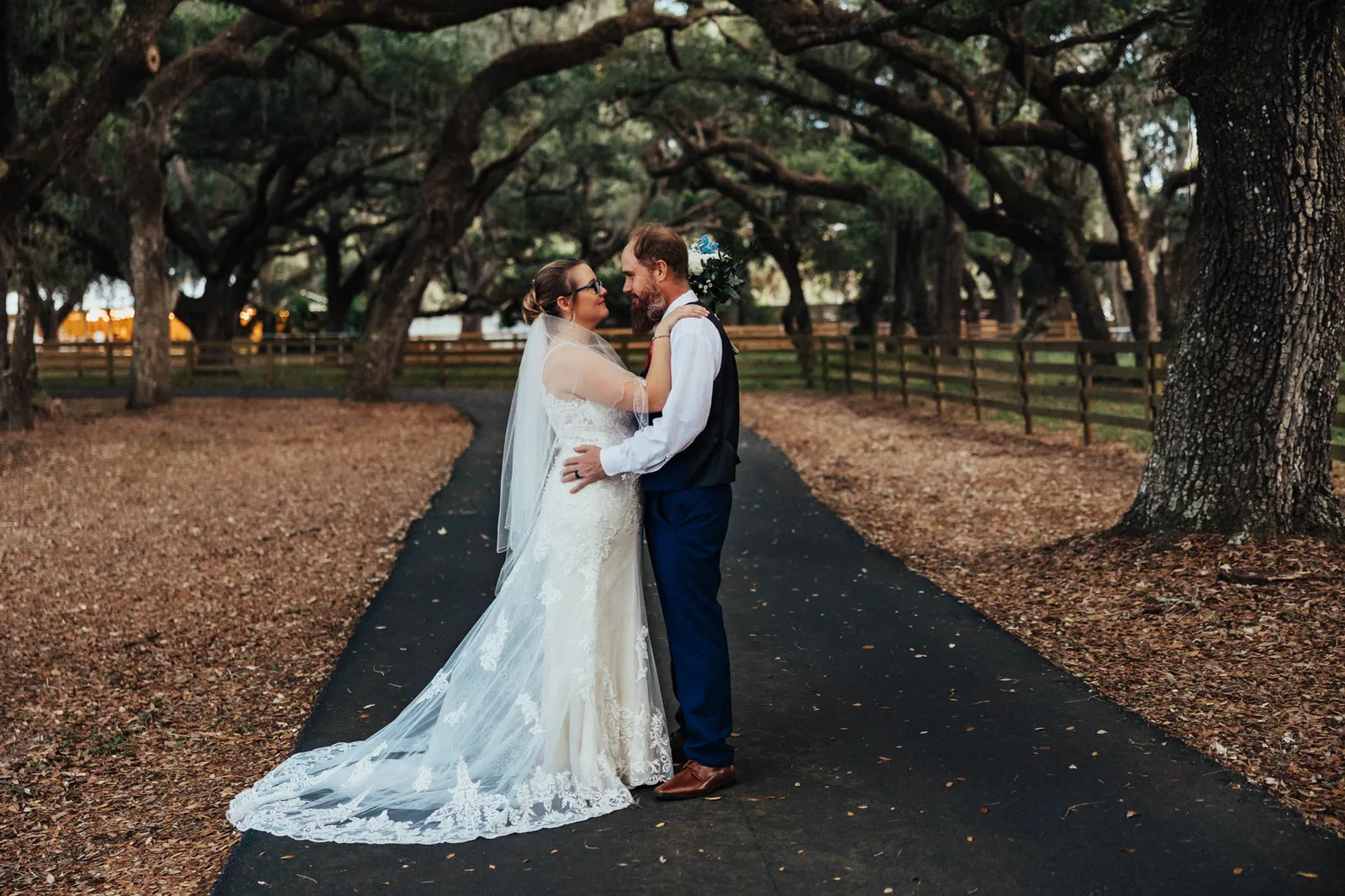 Bride and groom embracing on the drive, her lace train spread behind her