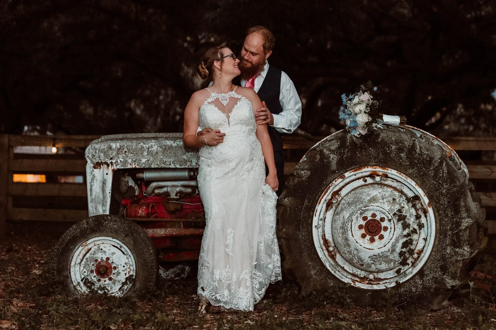 Bride and groom leaning against an old white tractor at dusk