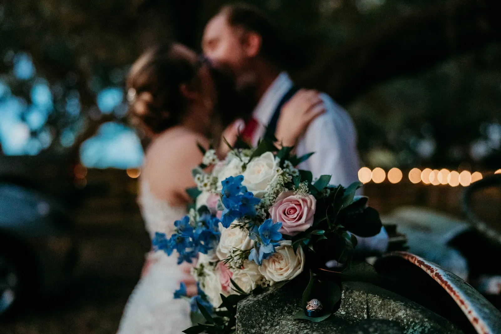 Bouquet in focus on the tractor as the groom kisses the bride's head behind it