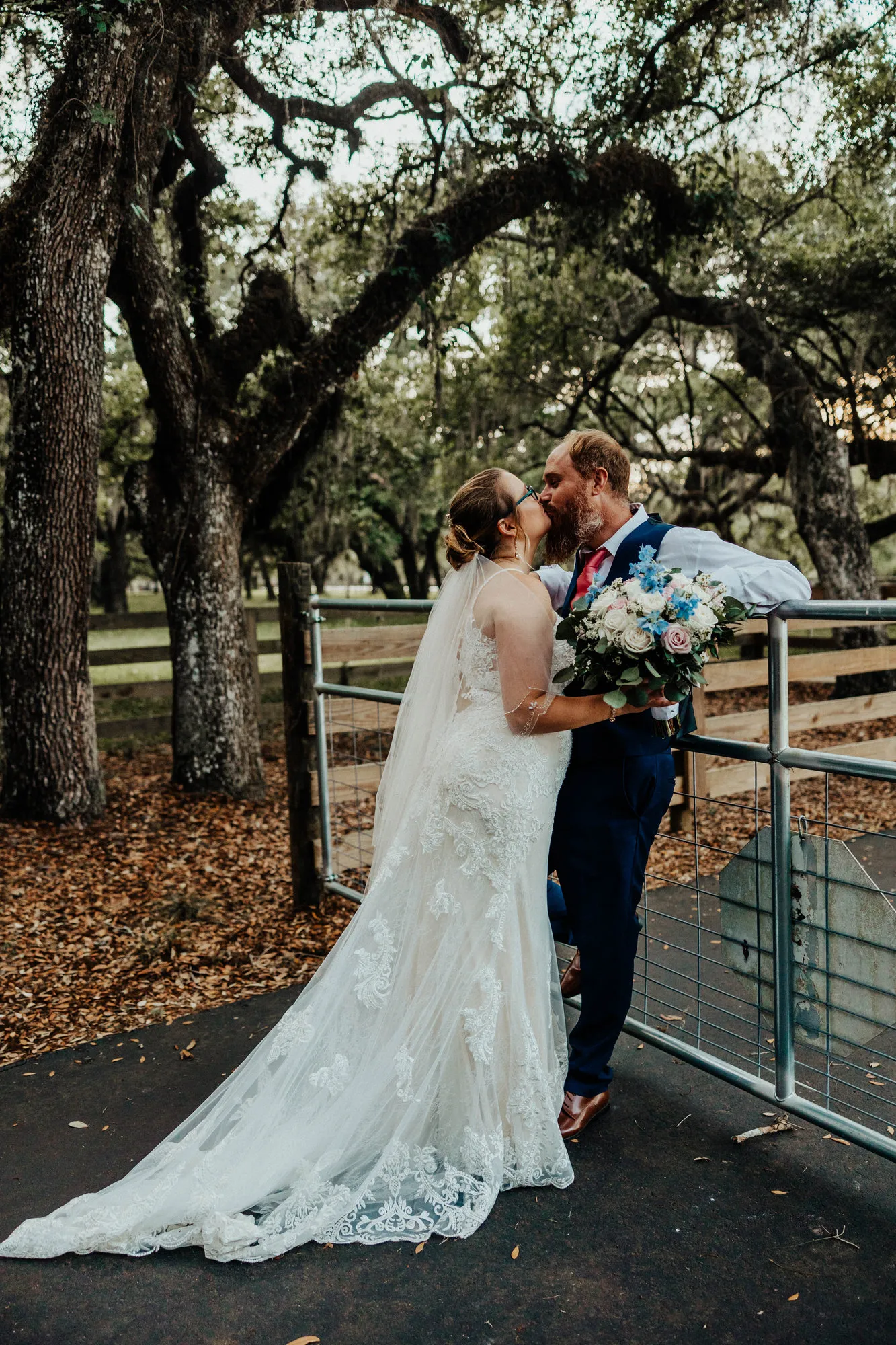 Bride and groom kissing by the paddock gate beneath the oaks