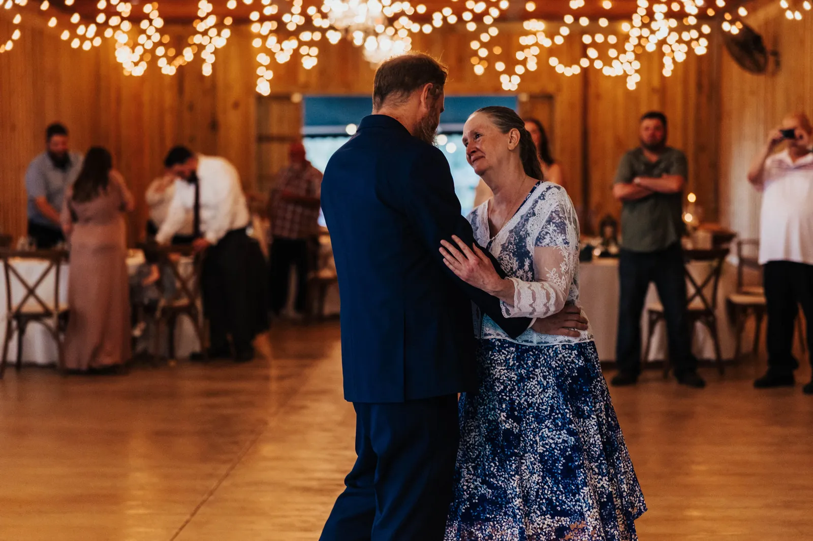 Groom dancing with a woman in a blue floral dress in the barn